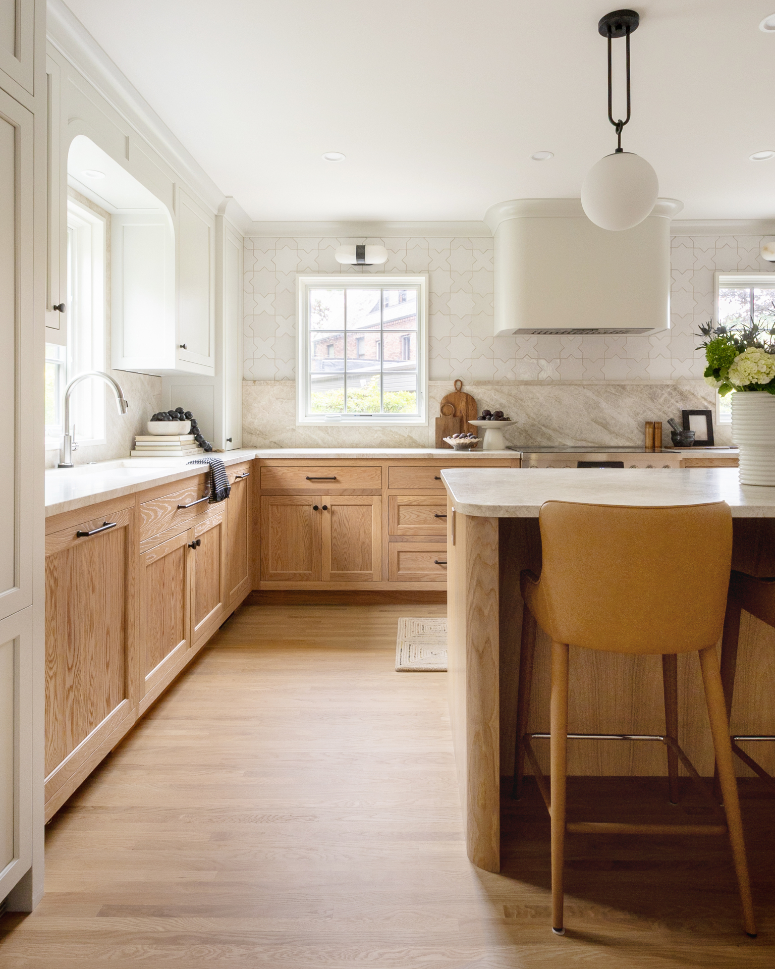 A Compass Studio kitchen with white oak cabinetry, a curved oak island, marble counters, star-and-cross tile backsplash, and a plaster range hood.