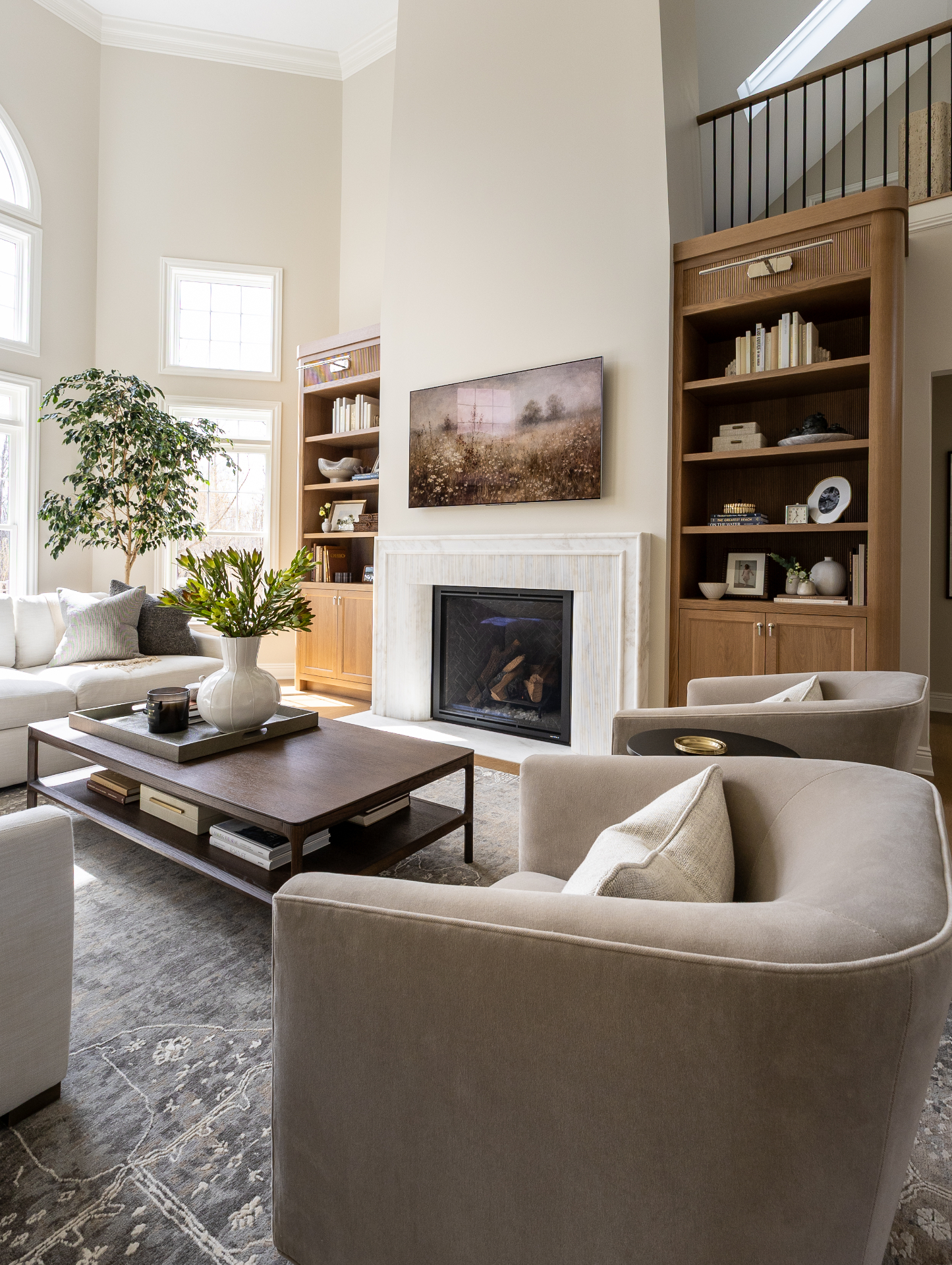 A Compass Studio living room with a double-height ceiling, white marble fireplace flanked by white oak built-ins, and soft linen seating.